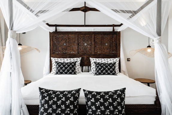 Mixed Charmed Life HOME Co. patterned pillows styled on white bedding and island-inspired decor.
