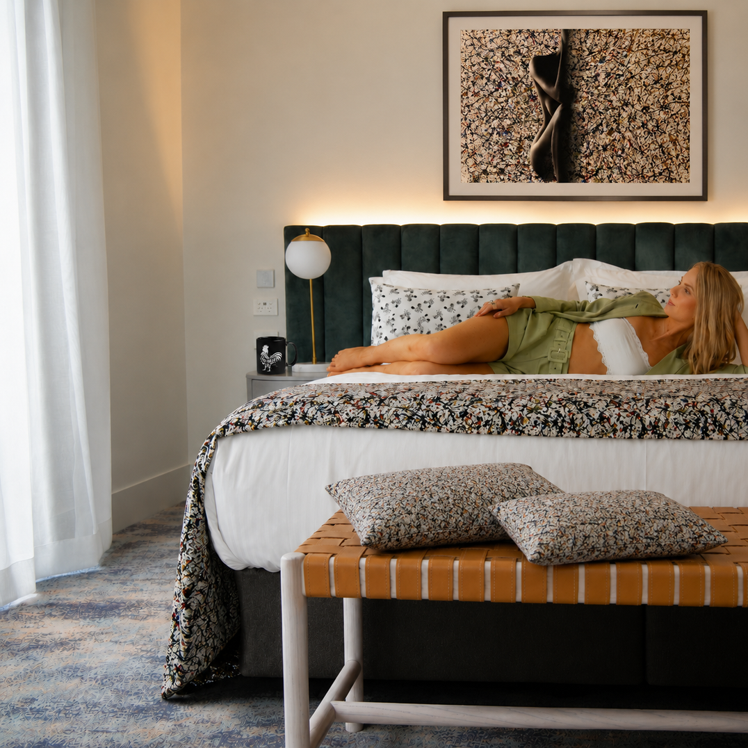 Charmed Life HOME Co. bedroom scene with artful pillows, patterned throw, framed wall art, and soft island-inspired luxury styling.