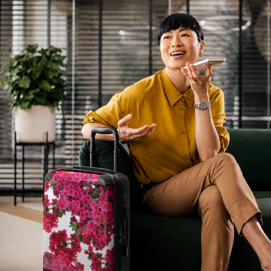 Two stylish women relaxing in an airport lounge with Charmed Life HOME Dancing Hibiscus high-top sneakers, floral hard-shell luggage, and a gold figure art-print suitcase.