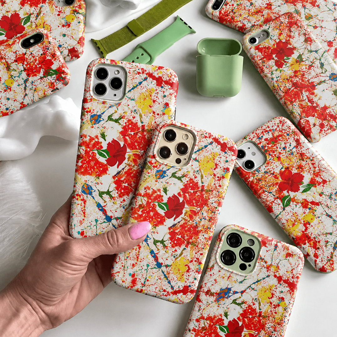 Collection of Charmed Life HOME Dancing Hibiscus tough cases for iPhone featuring red-orange paint splashes, red hibiscus flowers and green leaf accents.