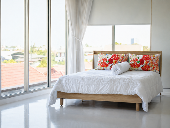 Bright luxury bedroom with Jewel’s Dancing Hibiscus Premium Pillow styled on white bedding near floor-to-ceiling windows.
